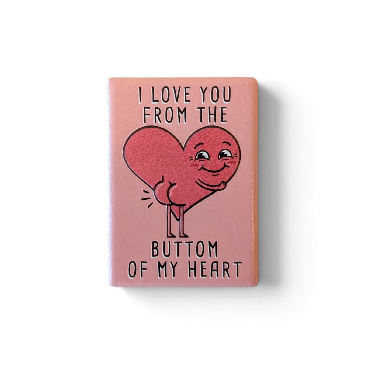 Rechteckiger Keramik-Kühlschrankmagnet (7x5 cm) mit seidenmatter Glasur in Altrosa. Abgebildet ist der schwarze Schriftzug 'I LOVE YOU FROM THE BUTTOM OF MY HEART' mit einem lustigen Herz inklusive Po im fühlbaren 3D-Relief.