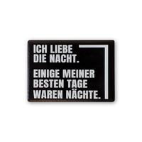 Rechteckiger Keramik-Kühlschrankmagnet (7x5 cm) im Querformat mit schwarzer, seidenmatter Glasur. Auf schwarzem Grund steht der weiße Schriftzug 'ICH LIEBE DIE NACHT. EINIGE MEINER BESTEN TAGE WAREN NÄCHSTE.' im fühlbaren 3D-Relief.