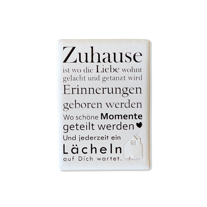 Rechteckiger Keramik-Kühlschrankmagnet (7x5 cm) mit seidenmatter Glasur. Auf hellem Grund steht der schwarze Spruch 'Zuhause ist wo die Liebe wohnt...' neben einer kleinen Haus-Illustration mit Herz im spürbaren 3D-Relief.