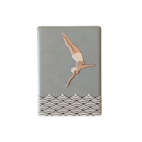 Rechteckiger Keramik-Kühlschrankmagnet (7x5 cm) mit seidenmatter Glasur in Salbeigrün. Zu sehen ist eine Turmspringerin im Art-Déco-Stil im Sprung über einem schwarz-weißen Wellenmuster im fühlbaren 3D-Relief.