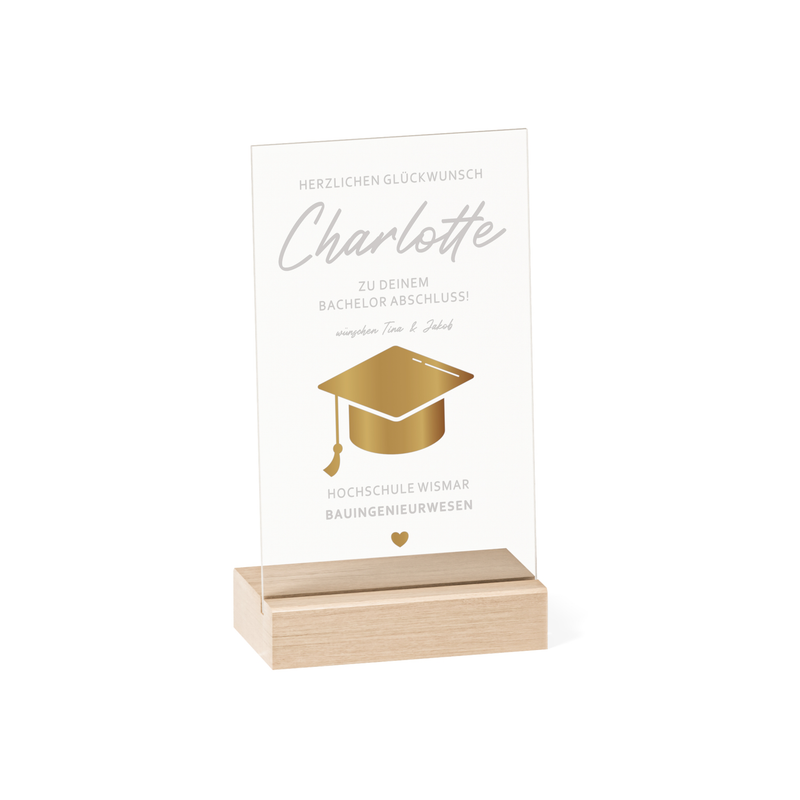 Transparenter Acrylglas-Aufsteller mit Holzsockel, personalisiert als Geschenk zum Abschluss. Zeigt goldene Doktorhut-Grafik, Namen, Studiengang und Hochschule in elegantem Design.