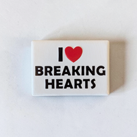 Rechteckiger Keramik-Kühlschrankmagnet (7x5 cm) im Querformat mit seidenmatter Glasur. Auf weißem Grund steht der schwarze Schriftzug 'I BREAKING HEARTS' mit einem leuchtend roten Herz-Symbol im fühlbaren 3D-Relief.