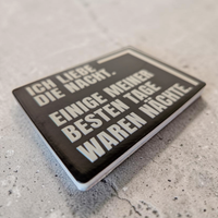 Rechteckiger Keramik-Kühlschrankmagnet (7x5 cm) im Querformat mit schwarzer, seidenmatter Glasur. Auf schwarzem Grund steht der weiße Schriftzug 'ICH LIEBE DIE NACHT. EINIGE MEINER BESTEN TAGE WAREN NÄCHSTE.' im fühlbaren 3D-Relief.