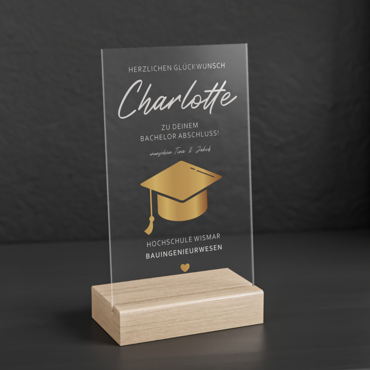 Transparenter Acrylglas-Aufsteller mit Holzsockel, personalisiert als Geschenk zum Abschluss. Zeigt goldene Doktorhut-Grafik, Namen, Studiengang und Hochschule in elegantem Design.