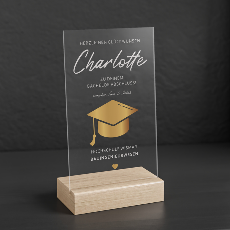 Transparenter Acrylglas-Aufsteller mit Holzsockel, personalisiert als Geschenk zum Abschluss. Zeigt goldene Doktorhut-Grafik, Namen, Studiengang und Hochschule in elegantem Design.