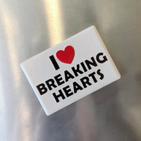 Rechteckiger Keramik-Kühlschrankmagnet (7x5 cm) im Querformat mit seidenmatter Glasur. Auf weißem Grund steht der schwarze Schriftzug 'I BREAKING HEARTS' mit einem leuchtend roten Herz-Symbol im fühlbaren 3D-Relief.