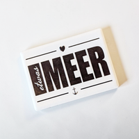 Rechteckiger Keramik-Kühlschrankmagnet (7x5 cm) im Querformat mit seidenmatter Glasur. Auf weißem Grund steht der schwarze Schriftzug 'etwas MEER' mit Anker und Herz-Symbol im fühlbaren 3D-Relief.
