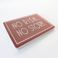 Rechteckiger Keramik-Kühlschrankmagnet (7x5 cm) im Querformat mit altrosafarbener, seidenmatter Glasur. Umrahmt von einer weißen Linie steht der Schriftzug 'NO RISK. NO STORY.' im fühlbaren 3D-Relief.