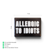 Rechteckiger Keramik-Kühlschrankmagnet (7x5 cm) im Querformat mit schwarzer, seidenmatter Glasur. Auf schwarzem Grund steht der weiße Schriftzug 'ALLERGIC TO IDIOTS' in doppelkonturierter Typografie im fühlbaren 3D-Relief.